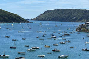 Harbour scene with boats in a bay, surrounded by green hills under a clear blue sky.
