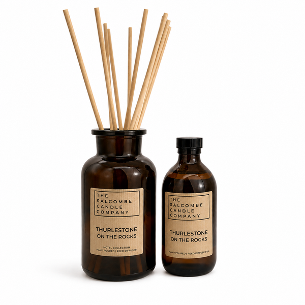 The Salcombe Candle Company Thurlestone on the Rocks reed diffuser set, featuring an amber glass bottle with natural wood reeds and a matching amber glass bottle with a black cap, on a white background.