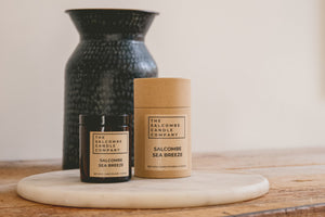 Two candles on a wooden surface with a black textured vase in the background.