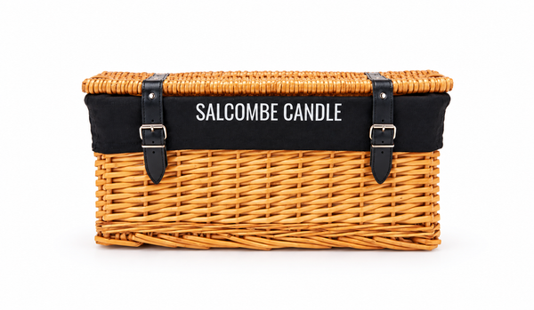 A rectangular wicker storage basket with a black fabric band across the top edge featuring the white text 'SALCOMBE CANDLE'. The basket has two black leather strap and buckle details on the front and is photographed against a solid white background.