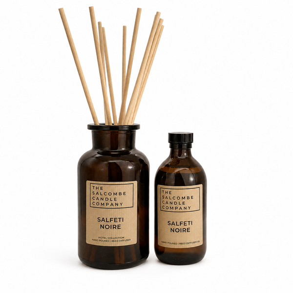 The Salcombe Candle Company Salfeti Noire reed diffuser set, featuring an amber glass bottle with natural wood reeds and a matching amber glass spray bottle, both with kraft paper labels, on a white background.