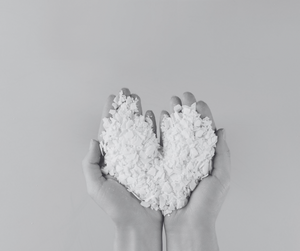 Two hands holding a heart-shaped pile of soy wax against a grey background